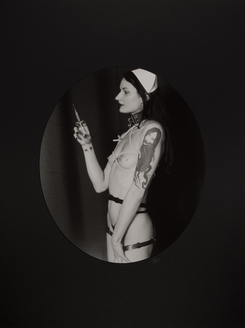 Magdalena Nurse II by Johnny Welch. Photograph of a semi-nude woman wearing a nurse's hat, choker, latex underwear, harness and tourniquet, holding a syringe
